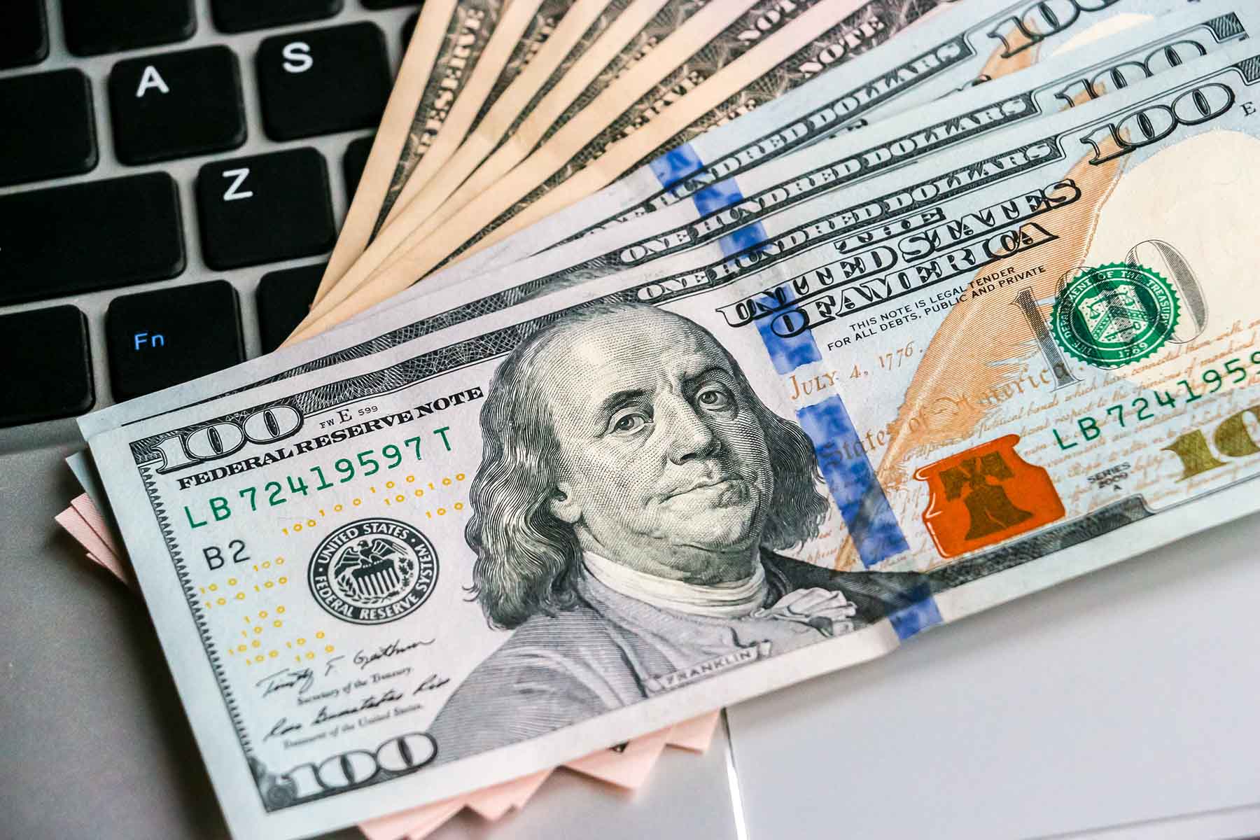 A stack of cash on top of a laptop keyboard.
