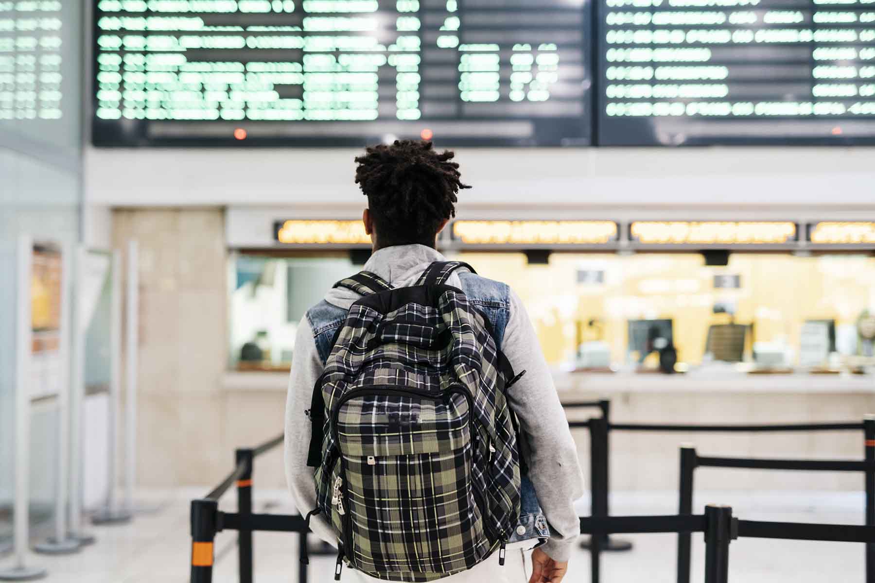 Young man standing in airport looking at board of destinations.