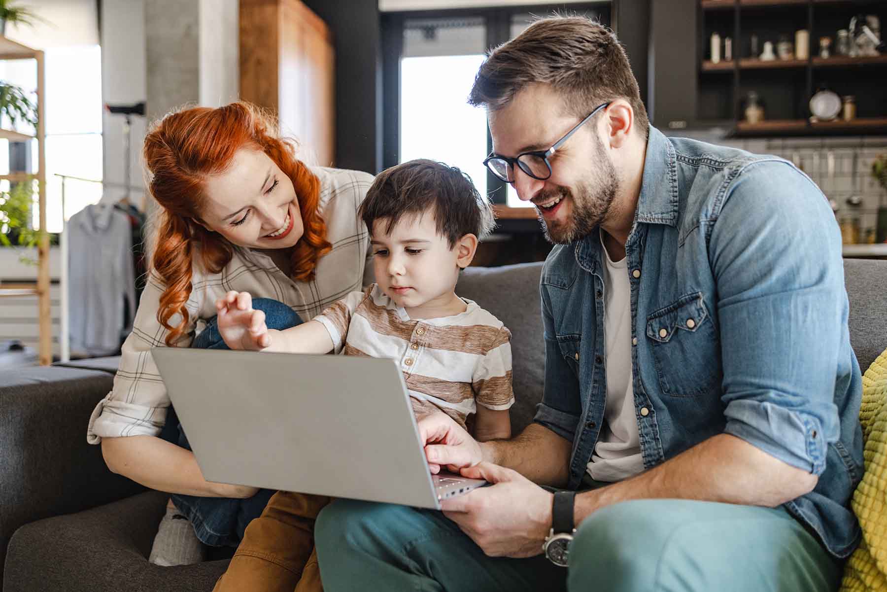 Mother, father, and son are using a laptop together on their couch.