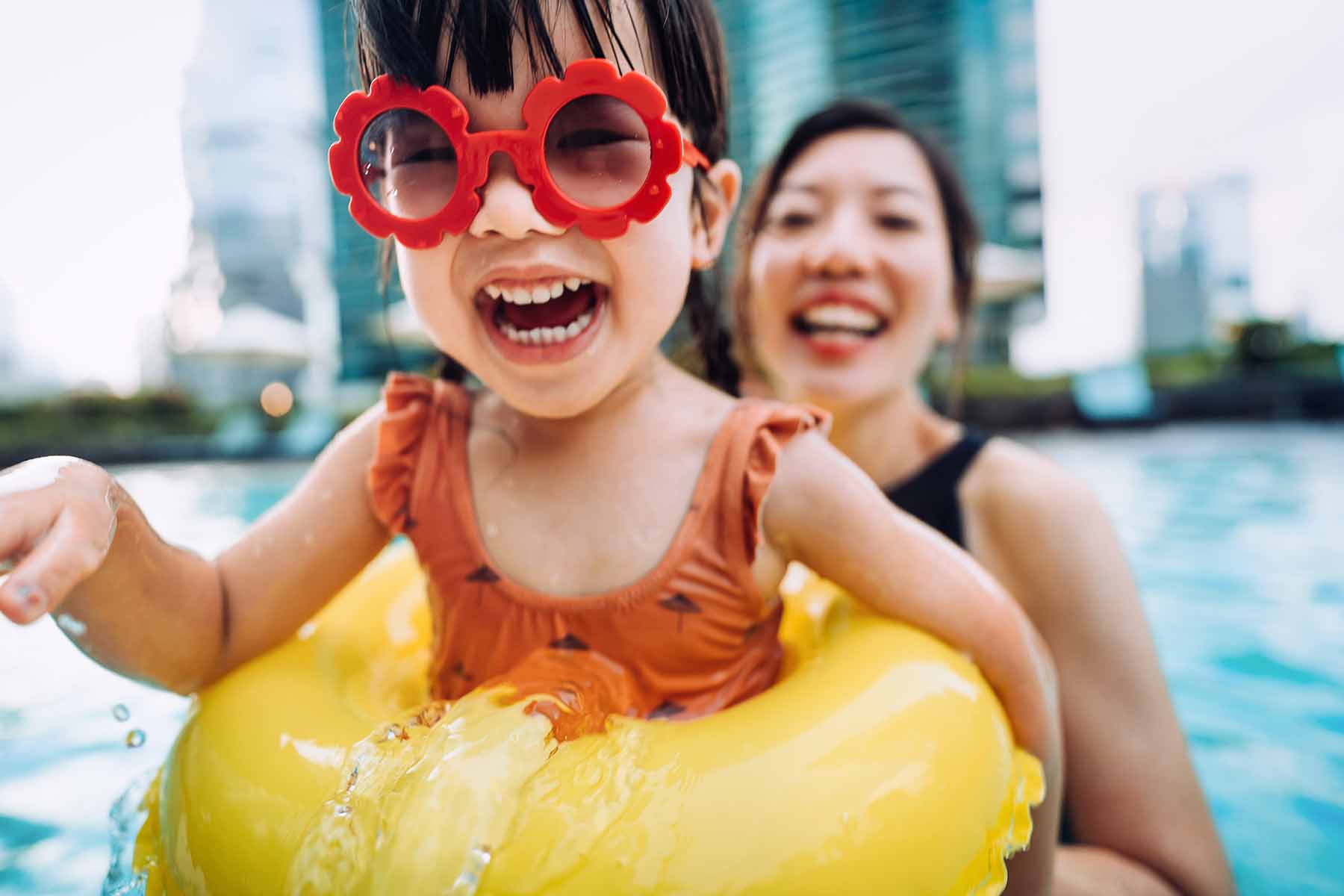 A young girl with sunglasses playing in the pool with her mother