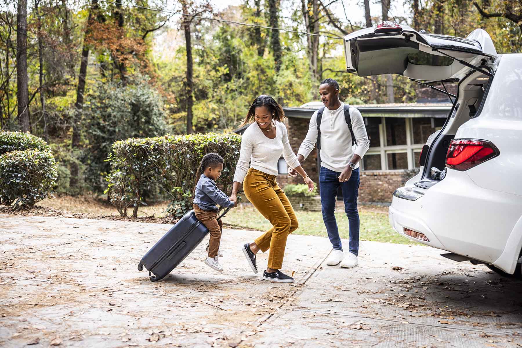 Mother pulling son on suitcase and loading car for family vacation