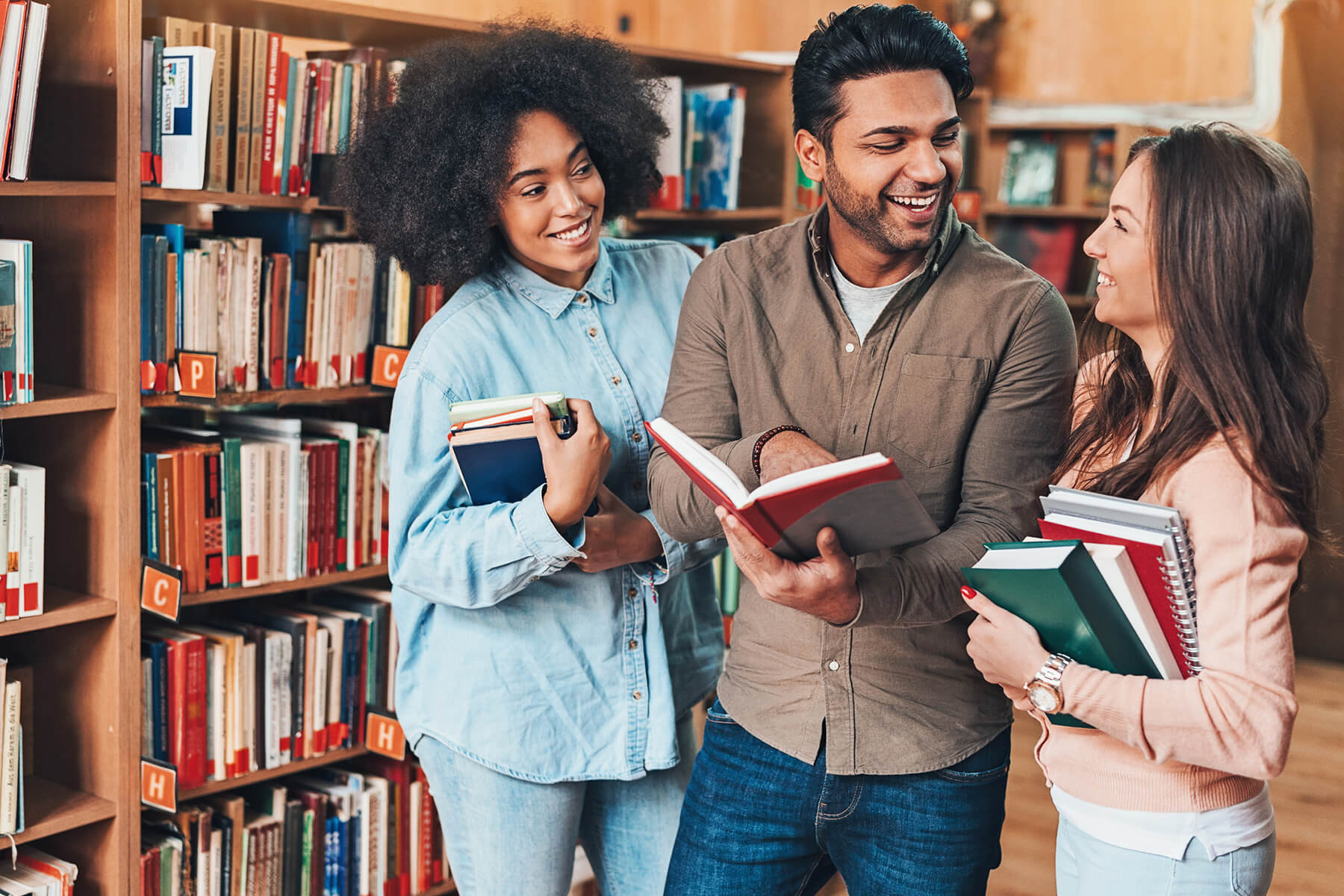 Three college students talk in a library while holding books