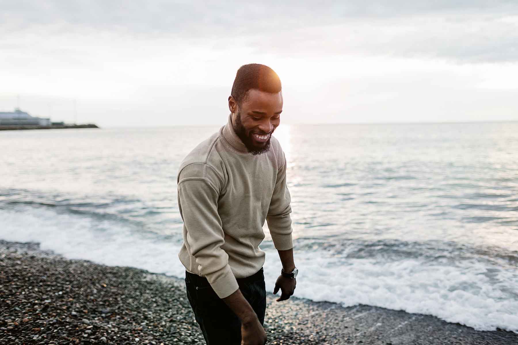Man walking along the beach shore, smiling and looking thoughtful.