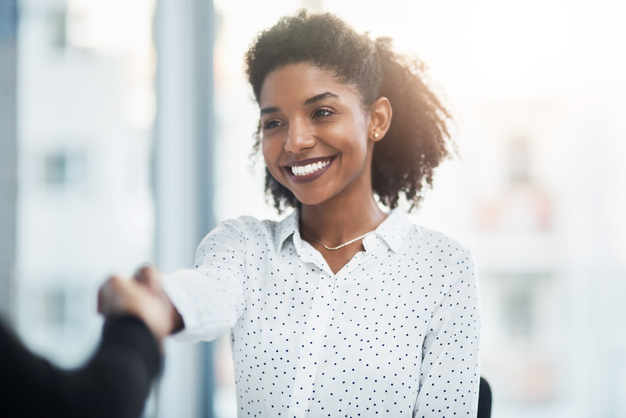 Smiling young businesswoman shakes a client's hand