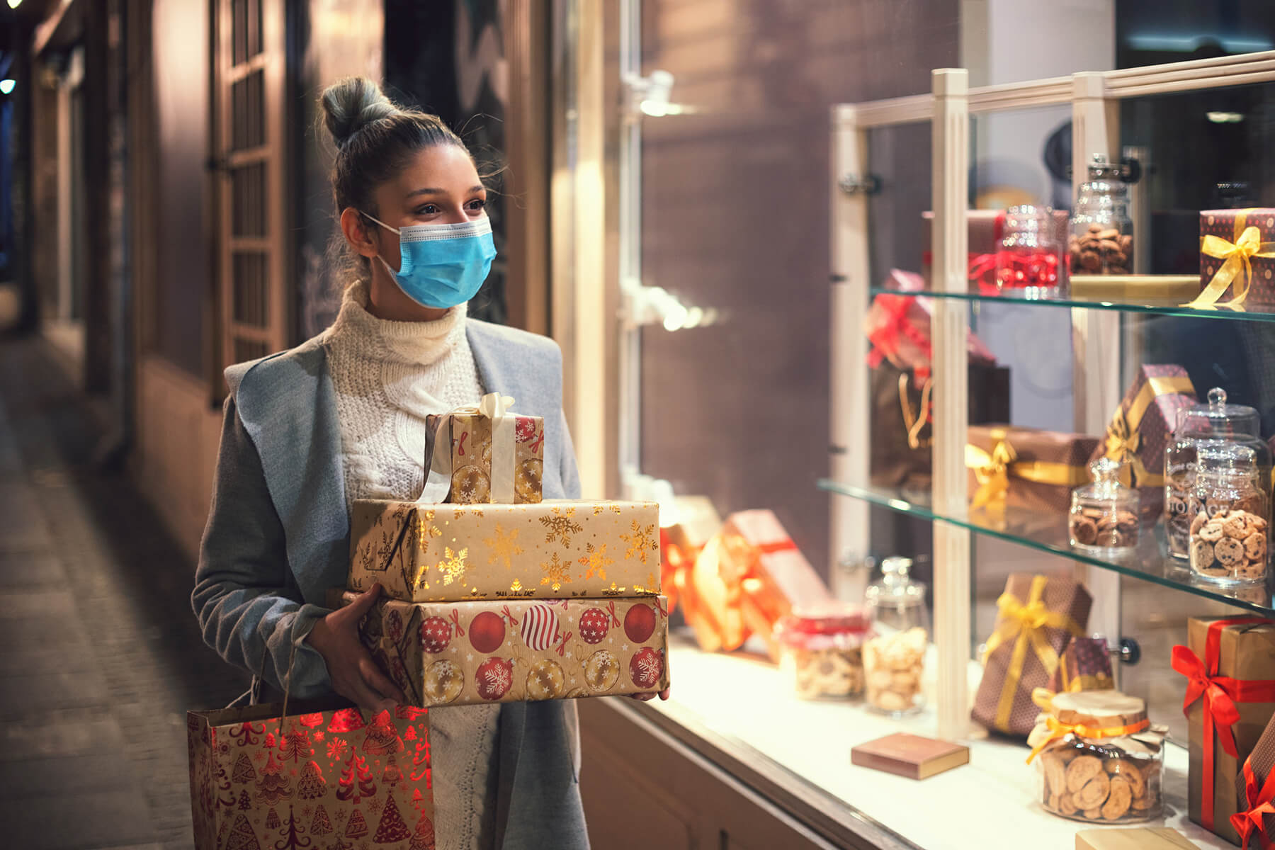 A woman wearing a facemask carries holiday gifts while window shopping