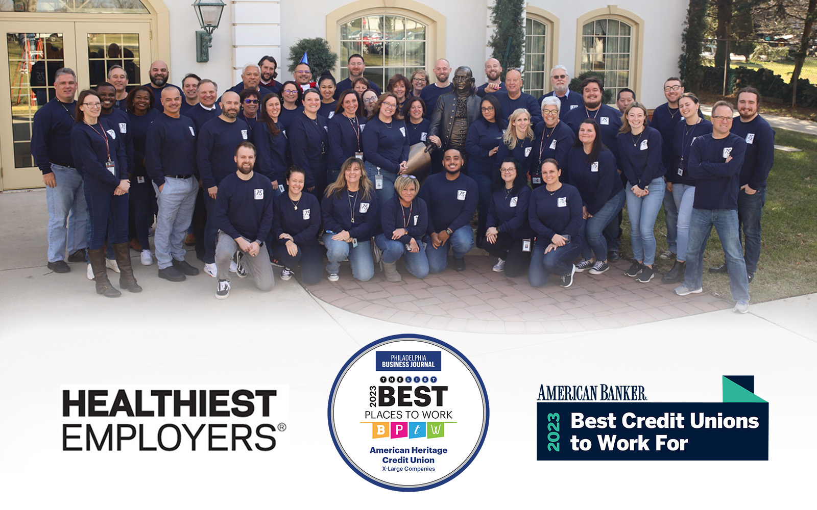 Group of American Heritage Credit Union associates stand in group with three award logos in the bottom third of the image,