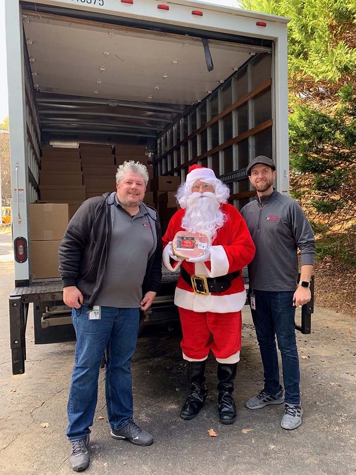 Volunteers stand in front of truck filled with food and meal donations for holiday season.