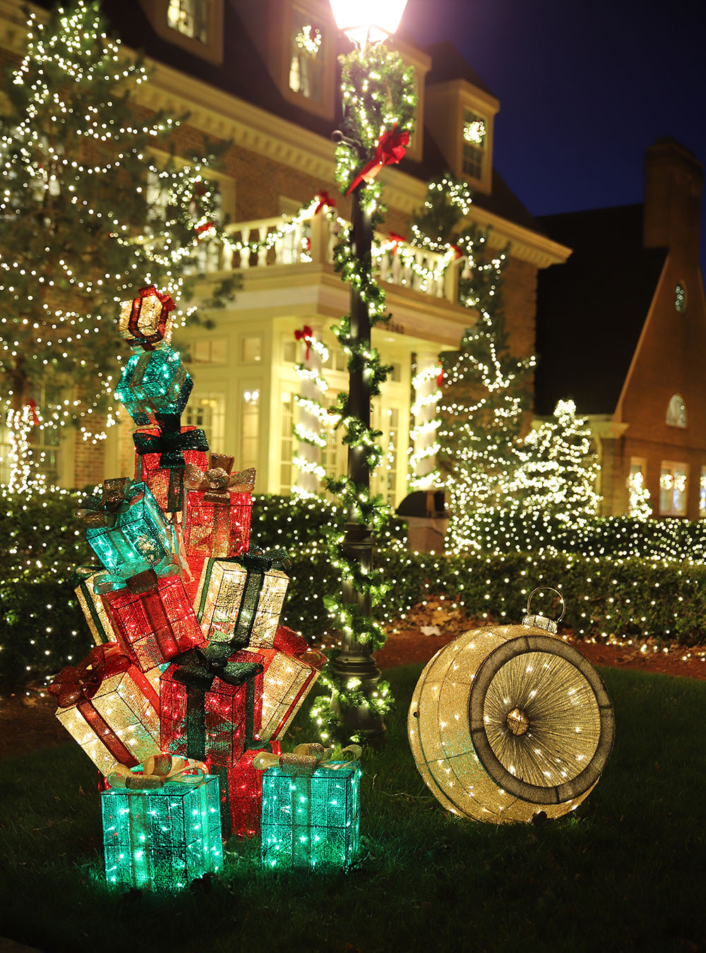 Presents and ornament decorative lights sit outside of an illuminated building.