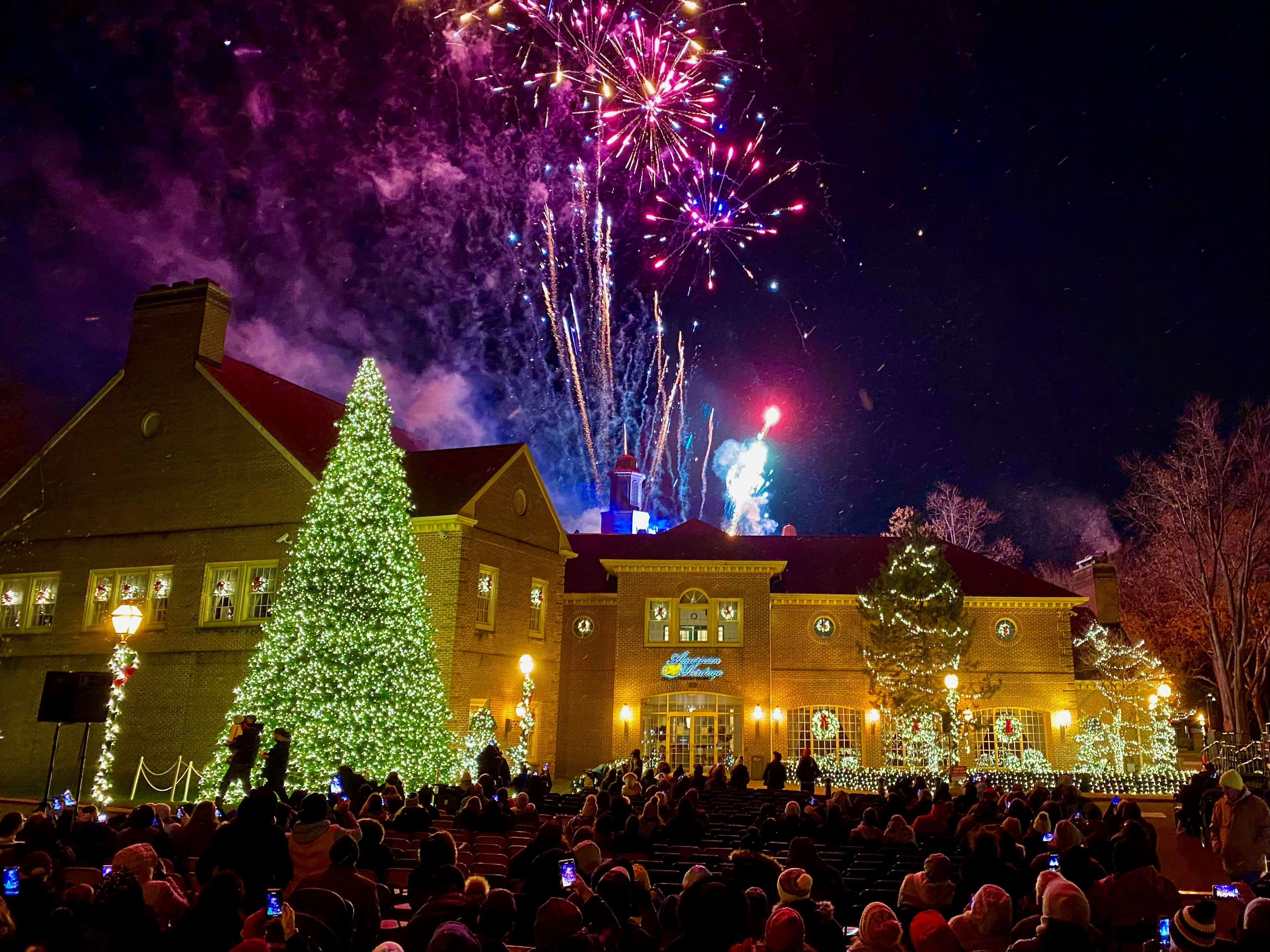 Fireworks light the sky behind an illuminated Christmas tree and building