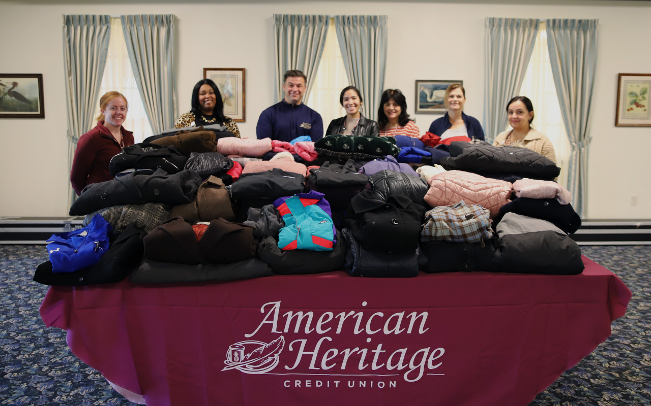 Volunteers stand behind tables piled with donated coats and jackets.